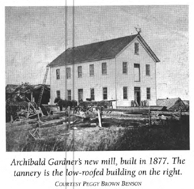 Black-and-white photo of a tall wooden building, Archibald Gardners mill, built in 1877. A low-roofed tannery is on the right. A wooden fence and a wagon are in the foreground. Courtesy of Peggy Brown Benson.